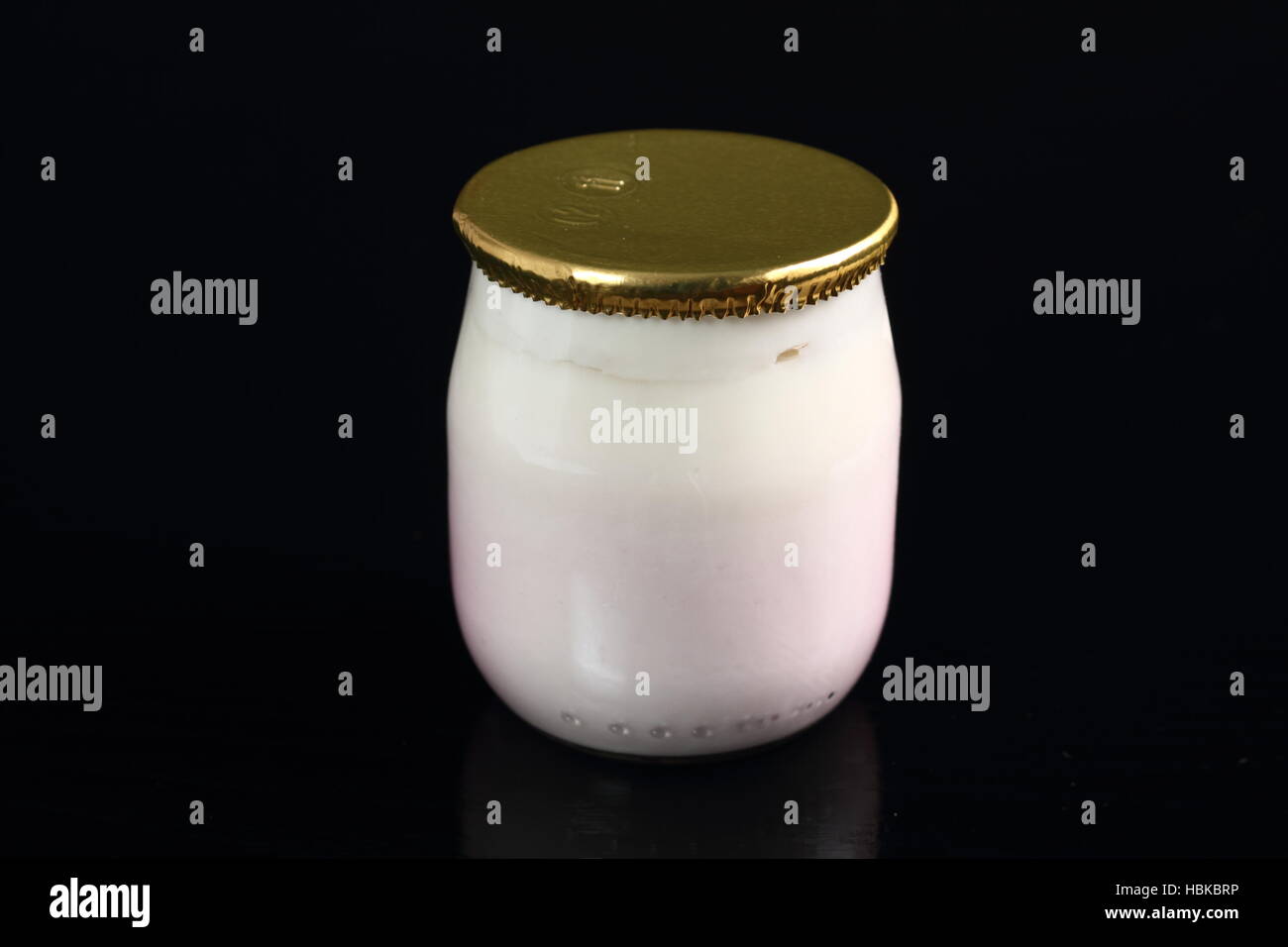 Yogurt in small glass jar with aluminium foil seal cap at black