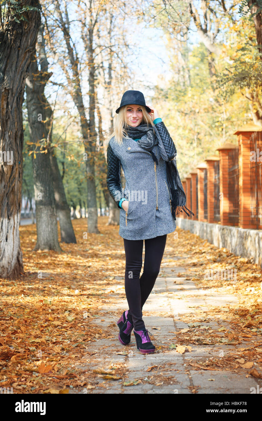 Gorgeous stylish young woman wearing fashionable clothes. Portrait of girl in black hat in the alley in the park. Stock Photo