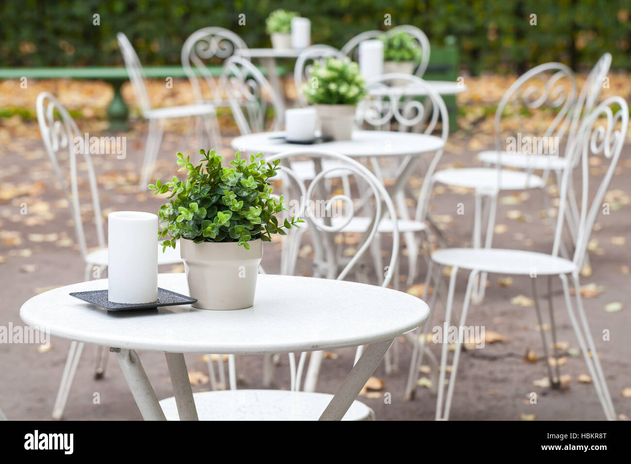 Outdoor cafeteria background interior, metal white chairs and tables with decorative green plants in pots and candles Stock Photo