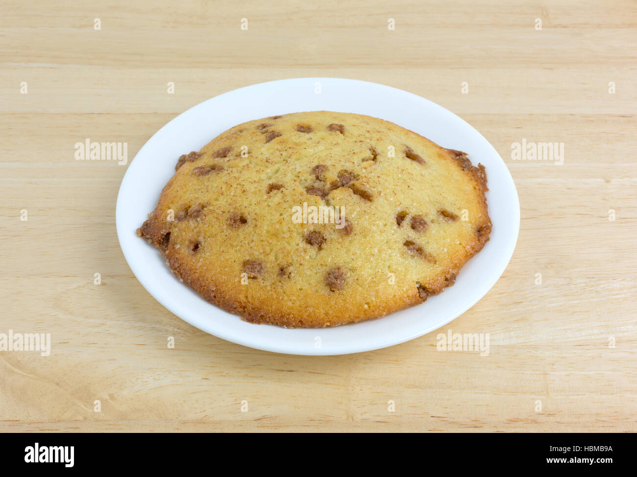 An apple spice muffin top on a white plate atop a wood table. Stock Photo