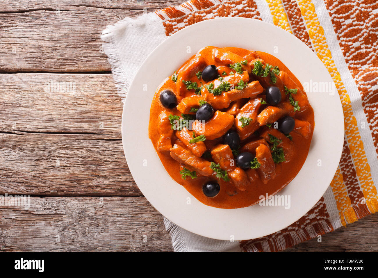Spanish pieces of pork stewed in a spicy sauce of wine, tomatoes and cream with black olives close-up on a plate. Horizontal view from above Stock Photo