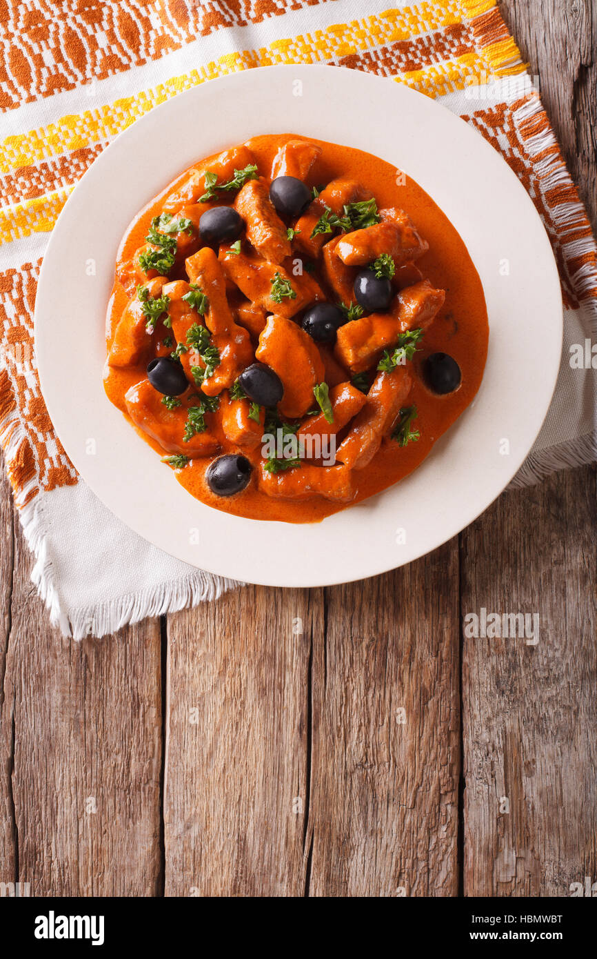 Spanish pieces of pork stewed in a spicy sauce of wine, tomatoes and cream with black olives close-up on a plate. vertical view from above Stock Photo
