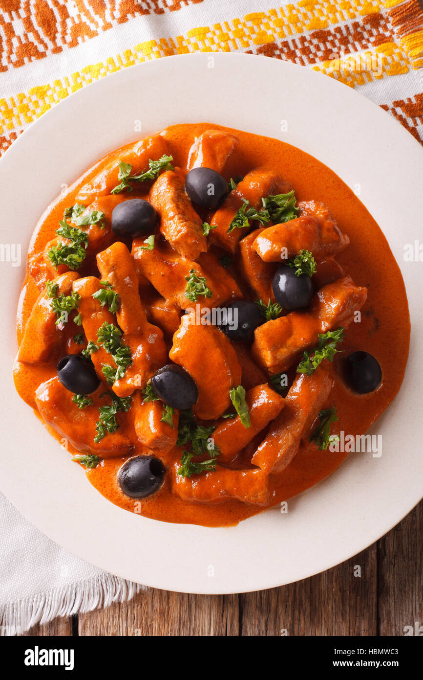 pork stew in a spicy sauce of wine, tomatoes and cream with black olives close-up on a plate. vertical view from above Stock Photo