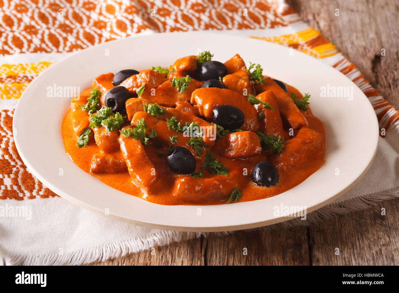 Spanish pieces of pork stewed in a spicy sauce of wine, tomatoes and cream with black olives close-up on a plate. horizontal Stock Photo