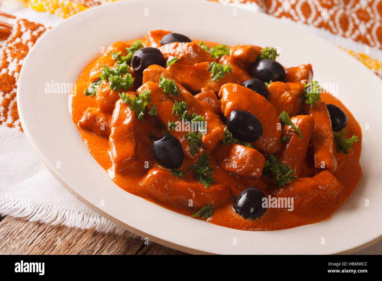 pork stew in a spicy sauce of wine, tomatoes and cream with black olives close-up on a plate. Horizontal Stock Photo