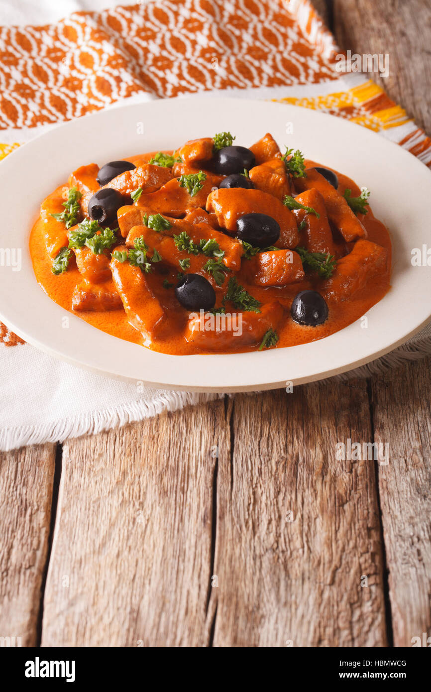 pork stew in a spicy sauce of wine, tomatoes and cream with black olives close-up on a plate. vertical Stock Photo