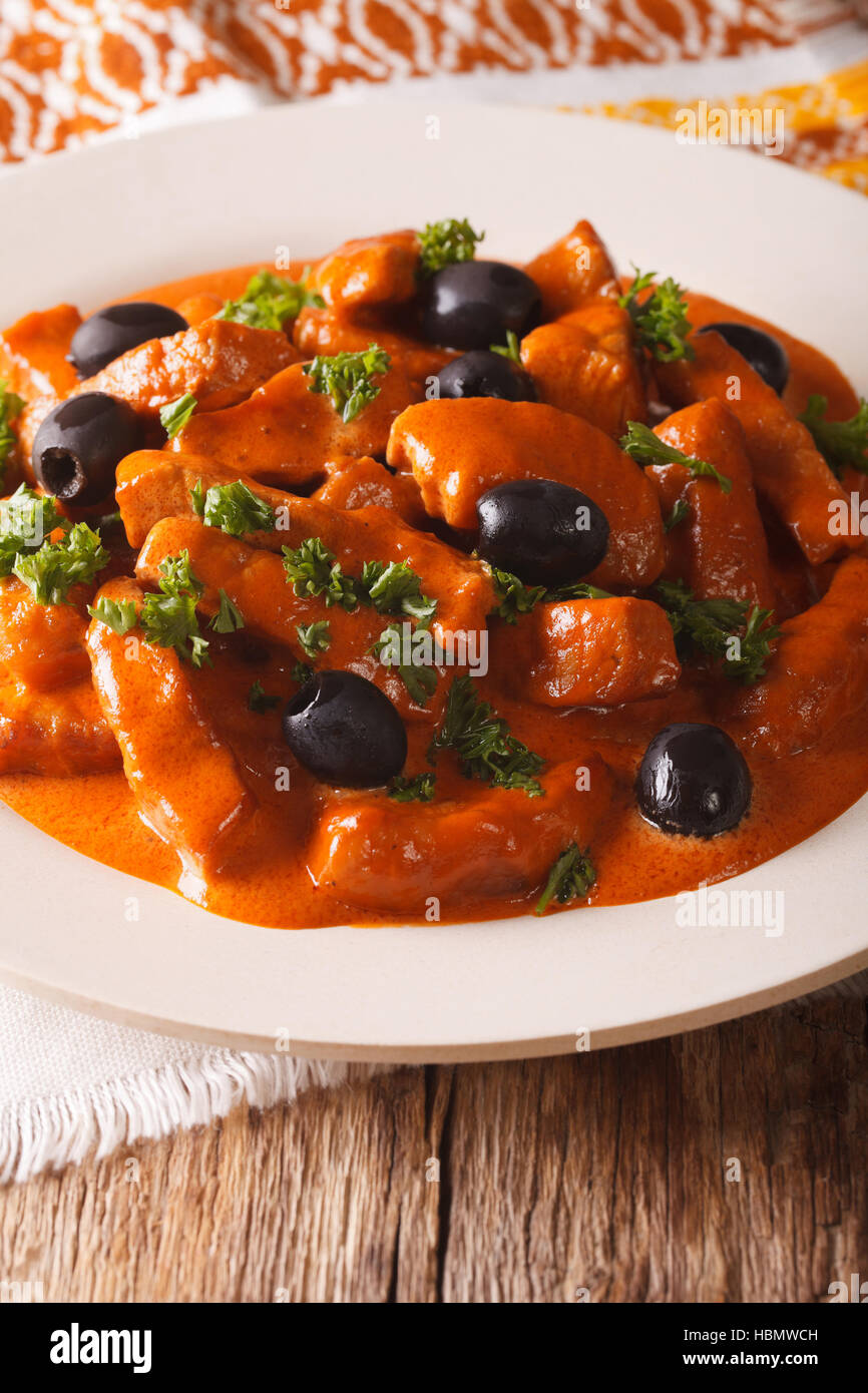 Spanish pork Raxo in a spicy sauce of wine, tomatoes and cream with black olives close-up on a plate. vertical Stock Photo