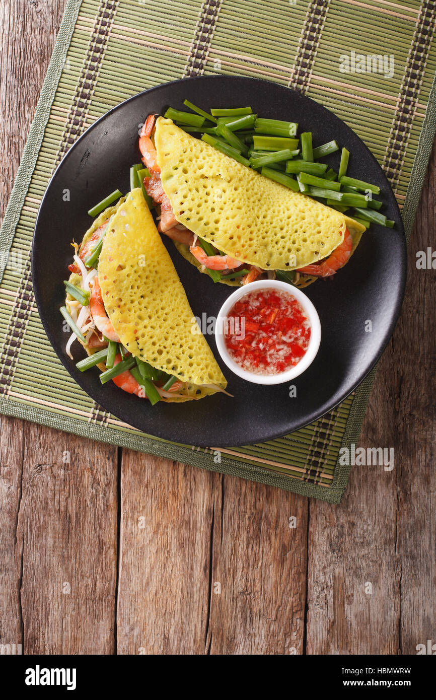 Vietnamese Banh Xeo crepes stuffed with pork, shrimp, onions and bean sprouts and a spicy sauce closeup on a plate on the table. vertical view from ab Stock Photo