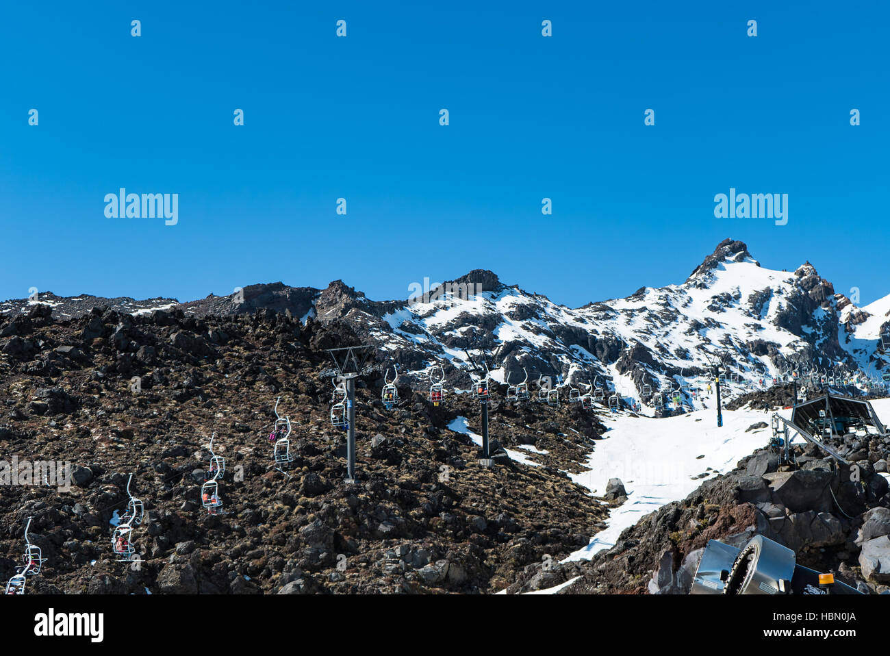 Skiers on ski lift over volcanic rock at Turoa Ski Area, New Zealand ...