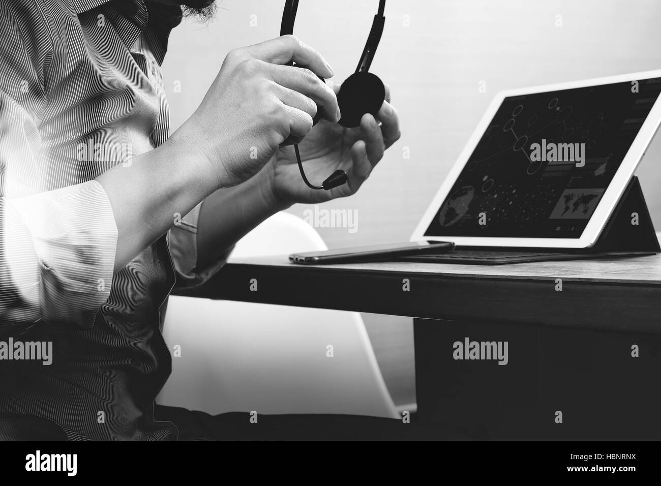 business man using VOIP headset with digital tablet computer docking smart keyboard, concept communication, it support,on wood desk,black white Stock Photo