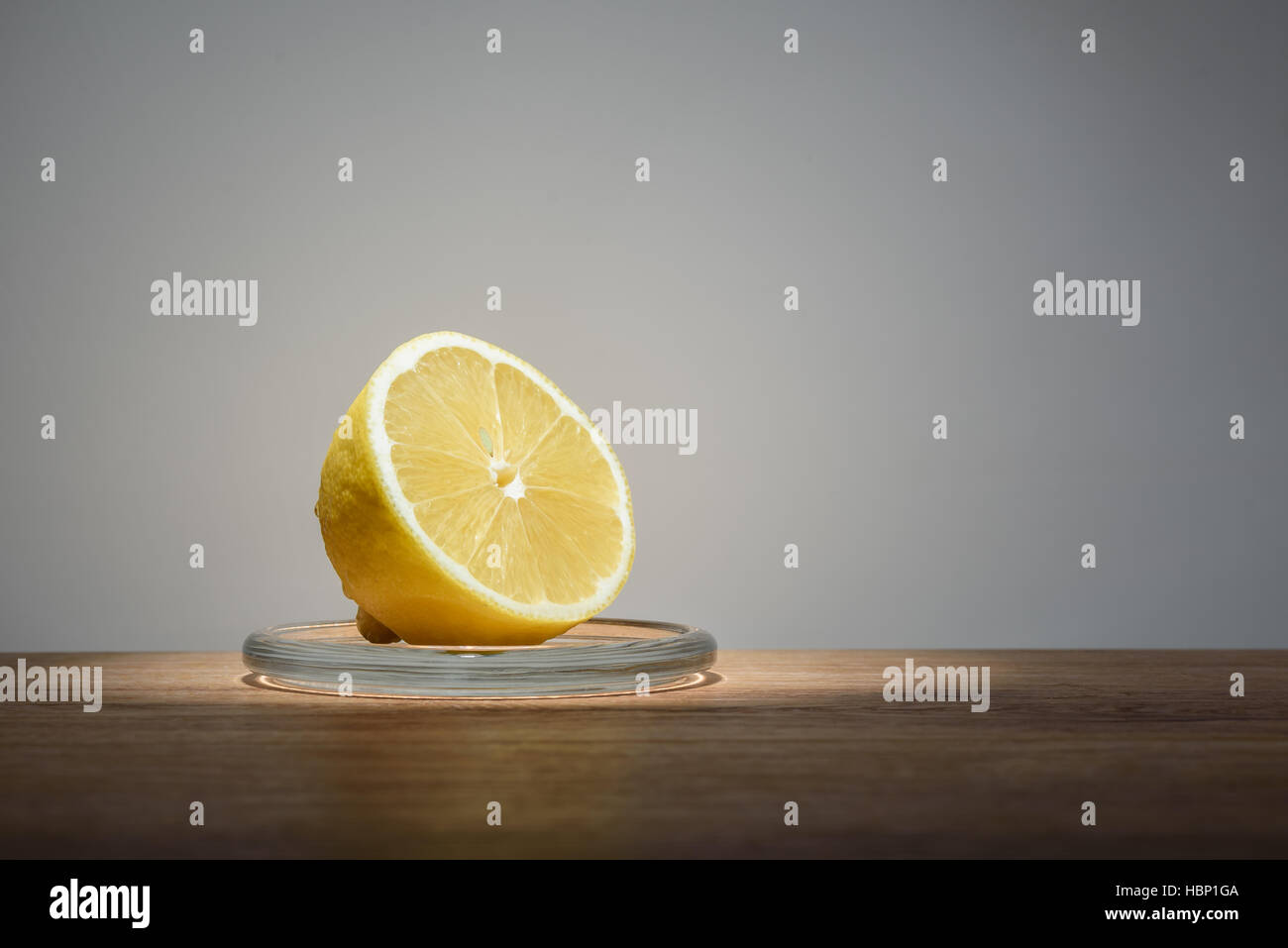 Juicy half a lemon in a glass dish on wooden table on light background Stock Photo