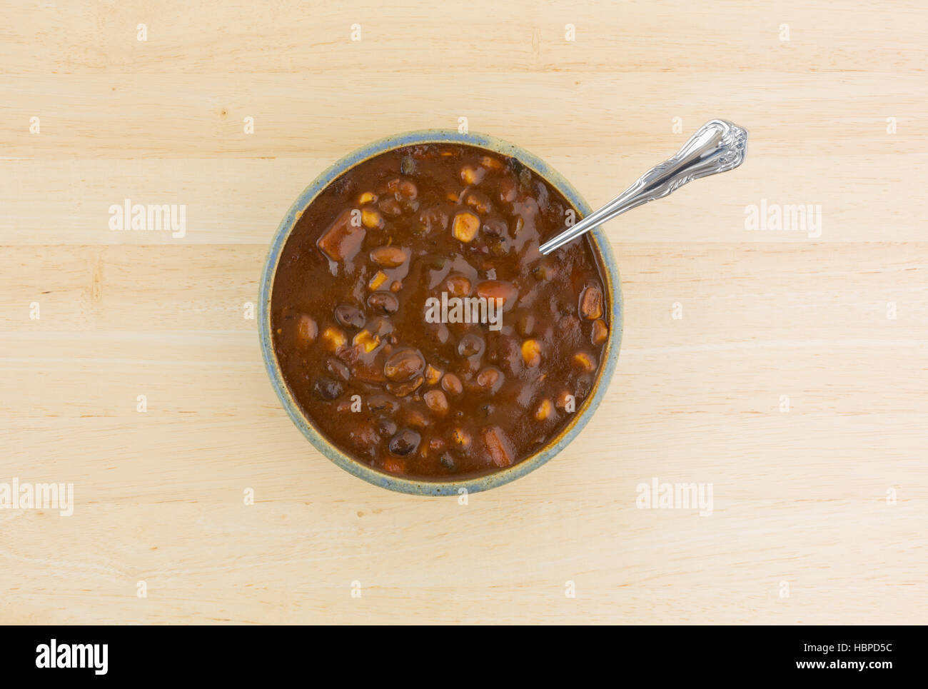 Top view of a bowl of vegetable three bean chili with  a spoon in the food atop a wood table top. Stock Photo