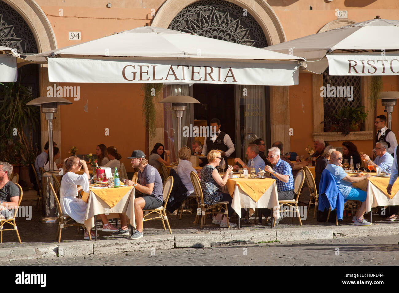 Piazza Navona, Rome, tourists dining at restaurant al fresco in the sunshine, with waiters Stock Photo