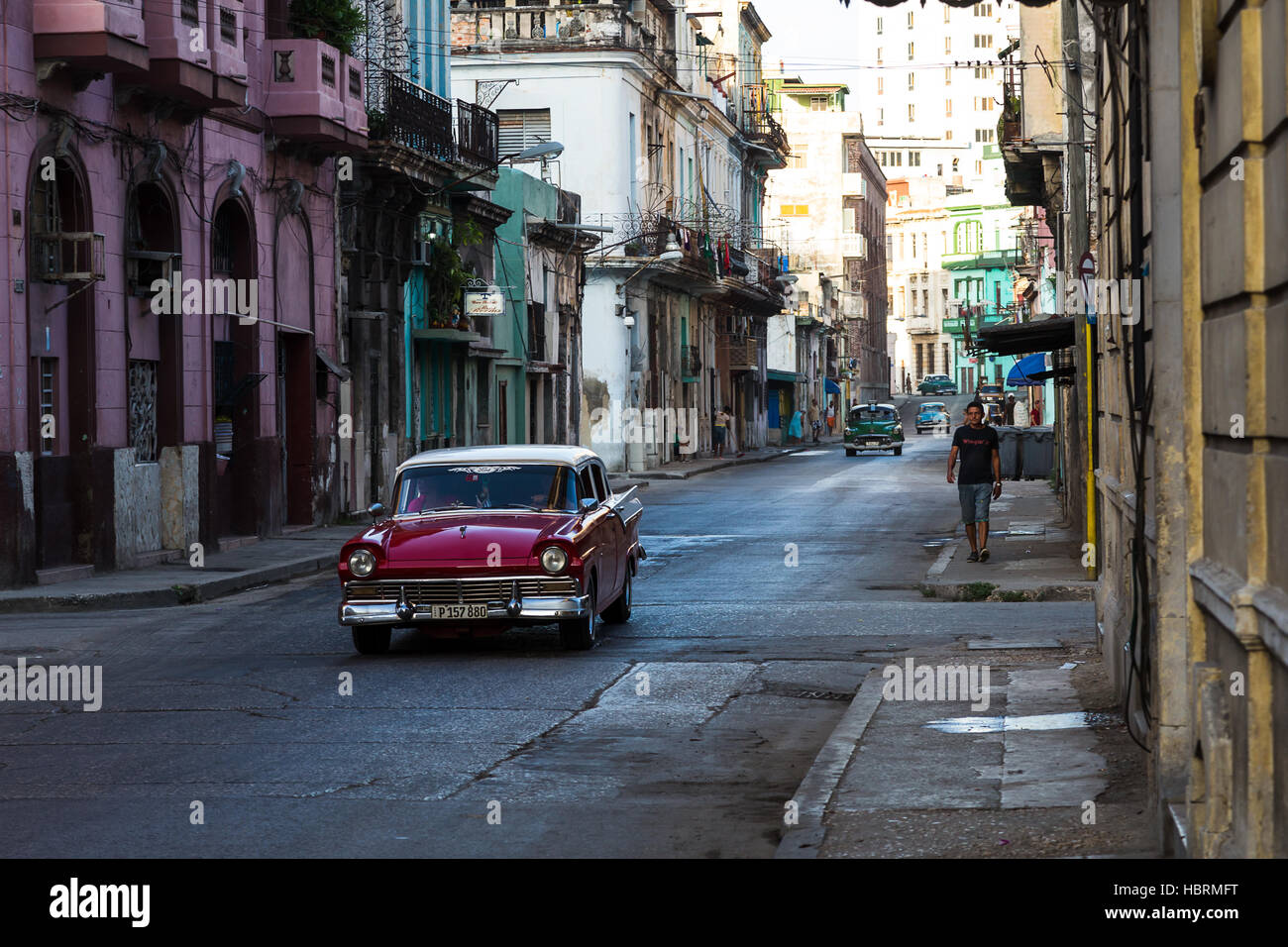 A red classical car traveling through the streets of Centro Habana early one morning. Stock Photo