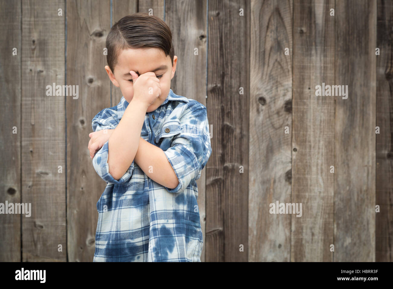 Young Frustrated Mixed Race Boy With Hand on Face Against Wooden Fence. Stock Photo