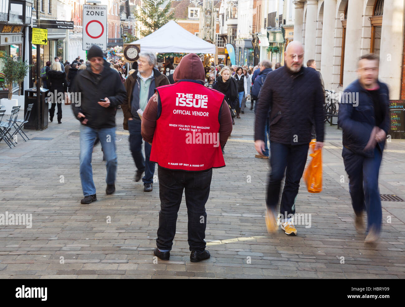 People walking past a Big Issue magazine vendor, Winchester, Hampshire, UK Stock Photo