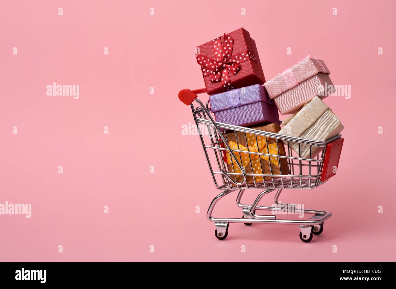 a shopping cart full of gifts of different colors on a pink background, with a negative space Stock Photo