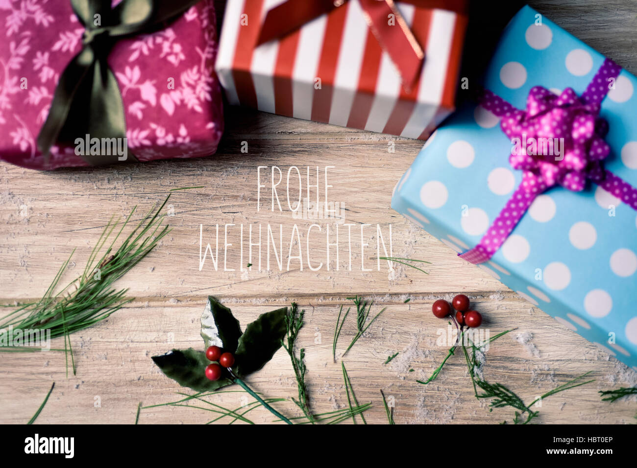 the text frohe weihnachten, merry christmas in german and some gifts wrapped in different papers and tied with ribbons of different colors, and some n Stock Photo