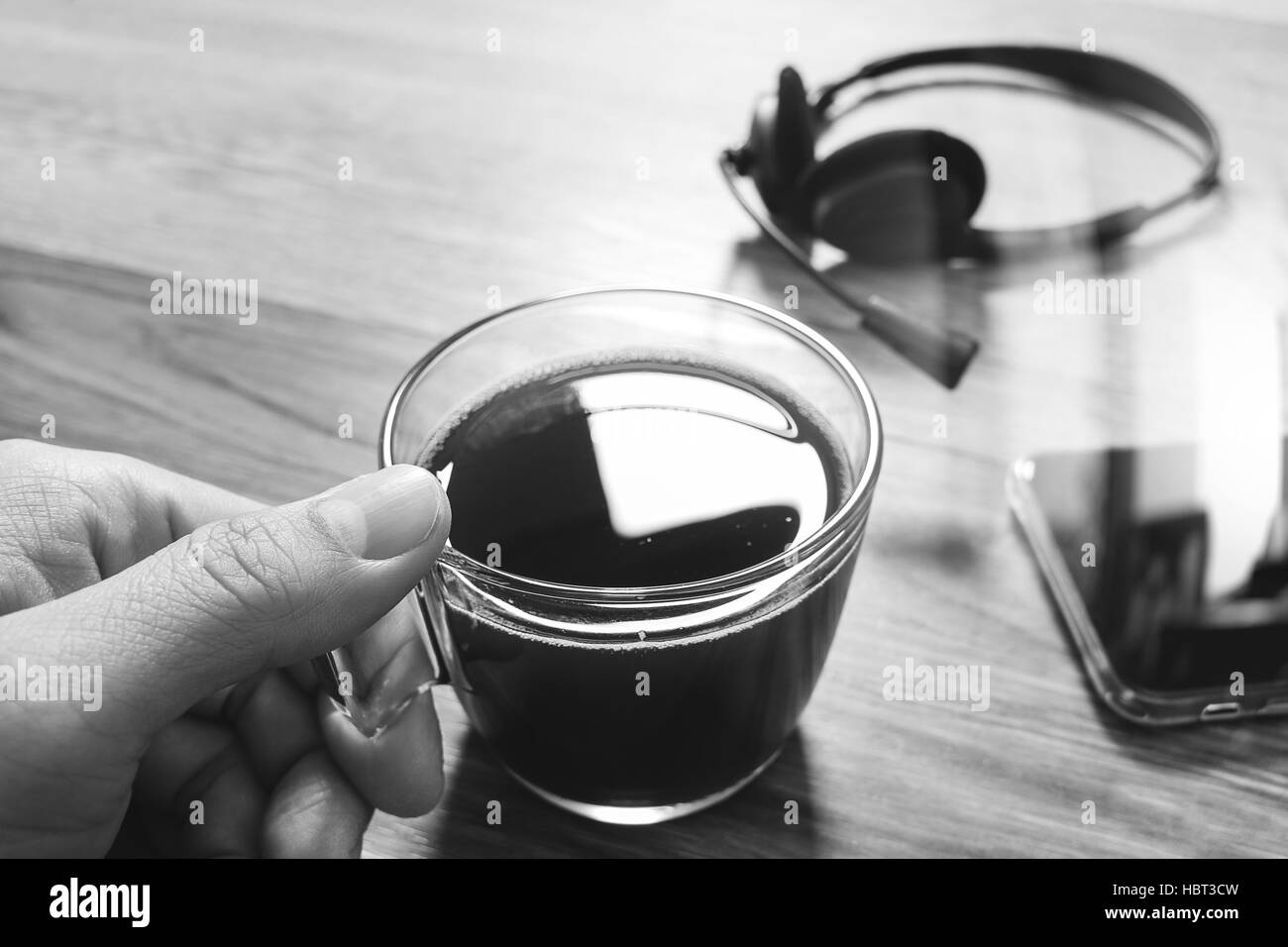 Hand holding Coffee cup or tea and voip headset,smart phone on wooden table,filter effect,black white Stock Photo