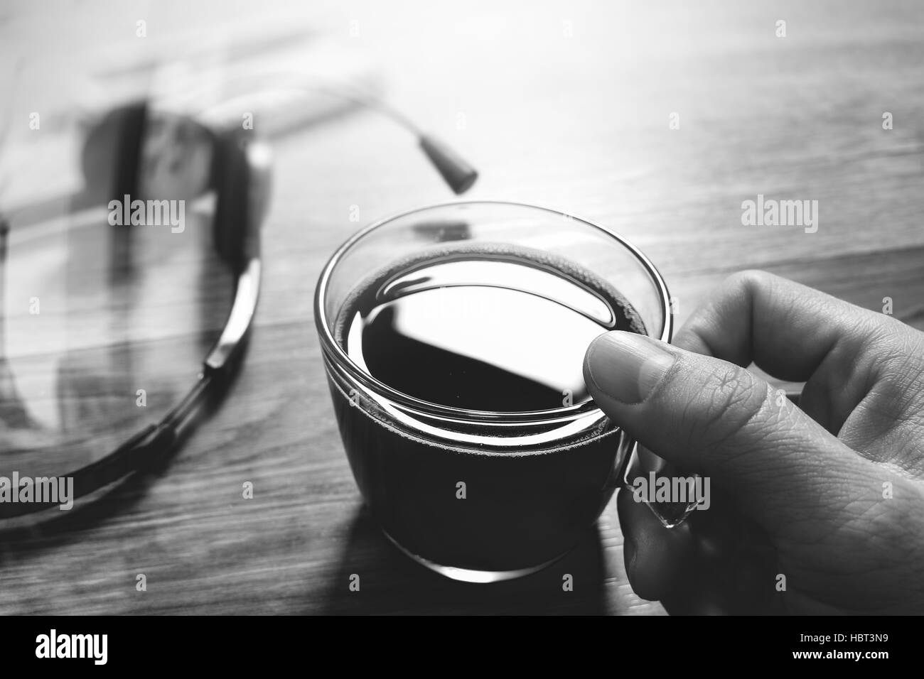 Hand holding Coffee cup or tea and voip headset,memo book on wooden table,filter effect,black white Stock Photo