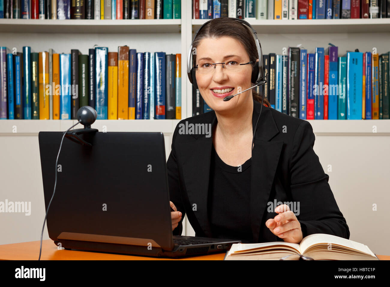 Smiling woman with headphone, computer and webcam in her office, consultant, adviser, teacher, online learning, business Stock Photo