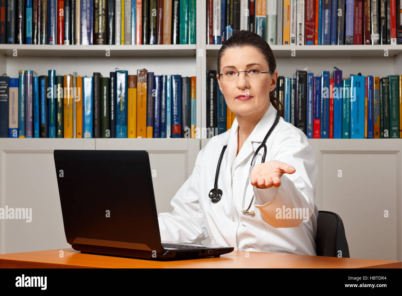 Doctor sitting at her desk in front of her computer and waiting with an outstretched hand  for money, pay, payment Stock Photo