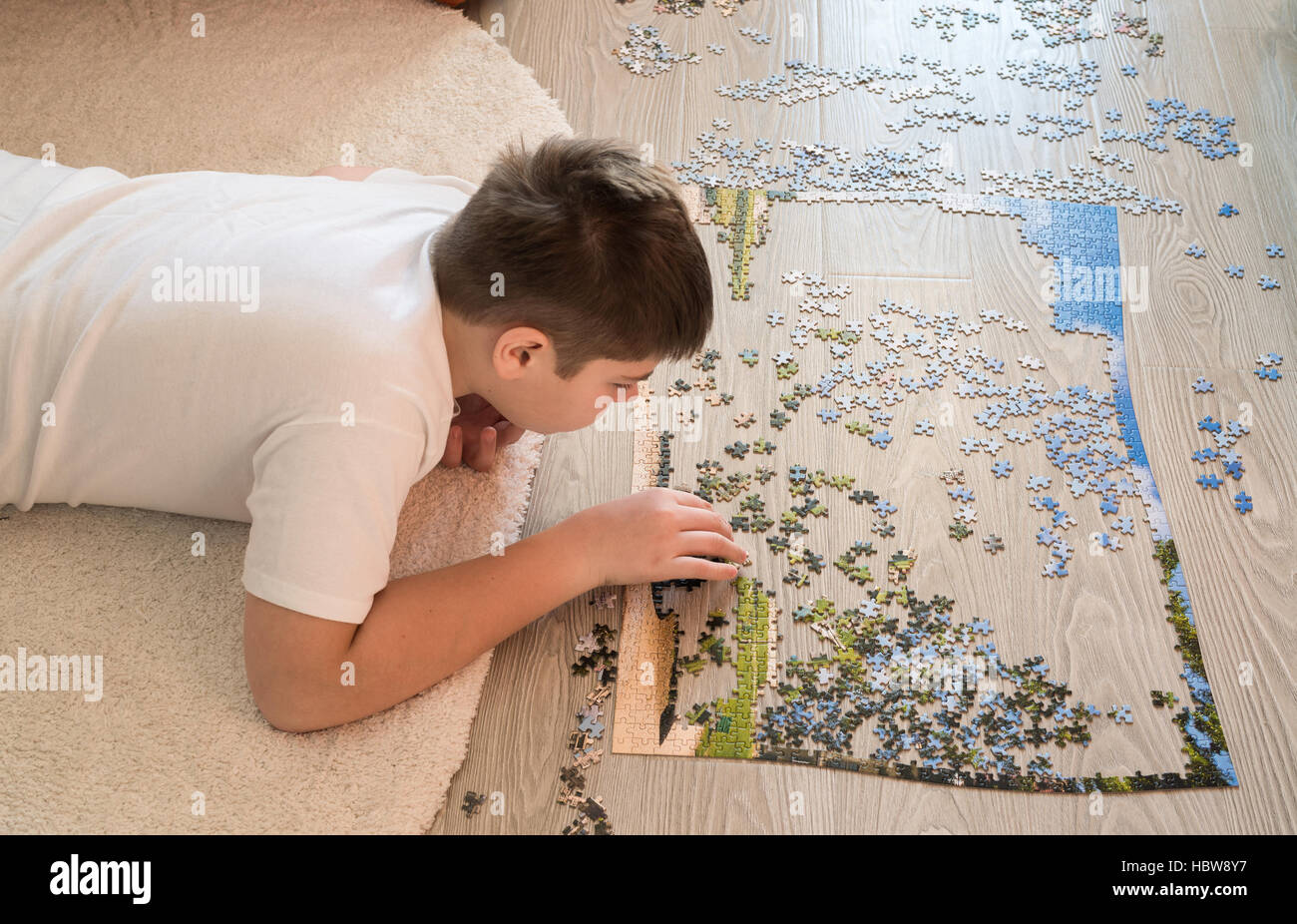 Teen boy collects a puzzle lying on carpet Stock Photo
