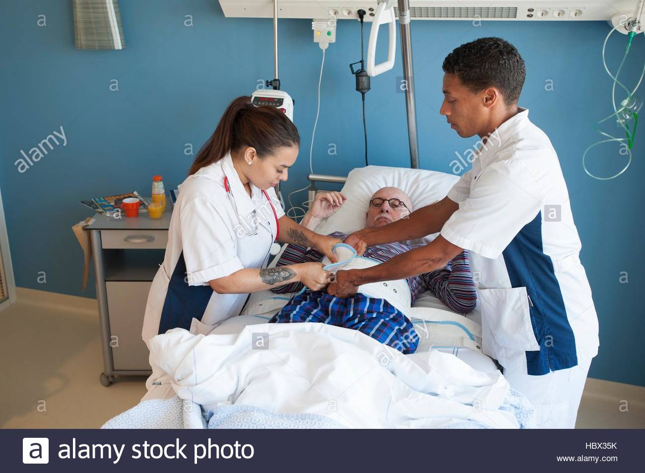 MODEL RELEASED. Two nurses fastening medical restraint to male Stock