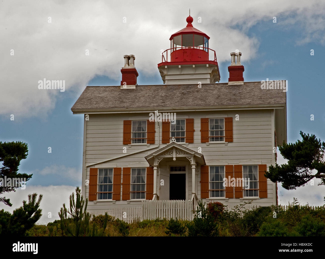 Two story white Lighthouse with yellow shutters and a red light housing in the middle of the roof.  Hillside facing the Pacific. Stock Photo
