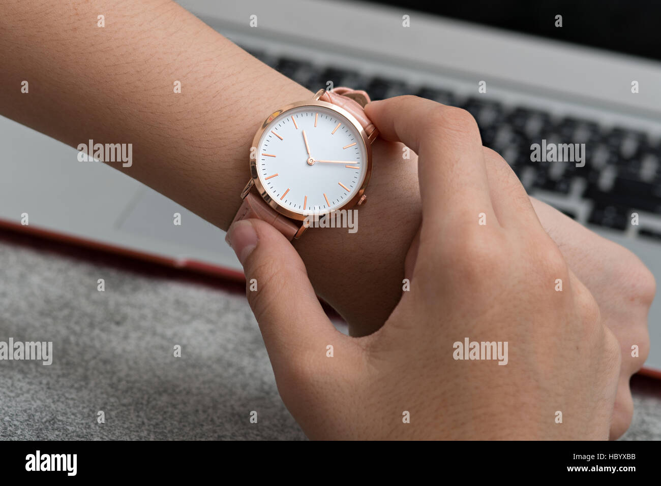 Girl's hand with wrist watch in front of desk with laptop computer Stock Photo