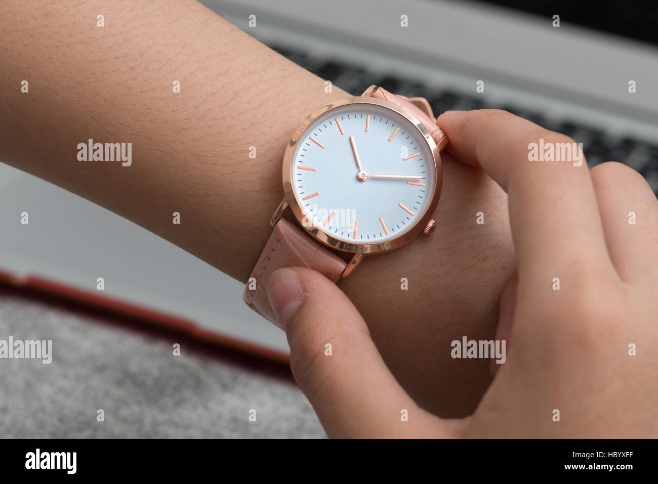 Girl's hand with wrist watch in front of desk with notebook computer Stock Photo