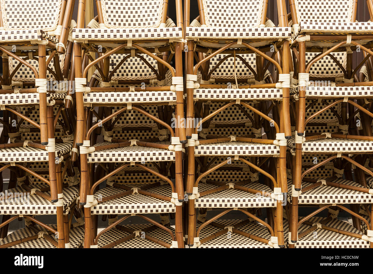 Close-up of stacks of several wicker bistro chairs on the sidewalk outside a café in Chicago, Illinois, USA. Stock Photo