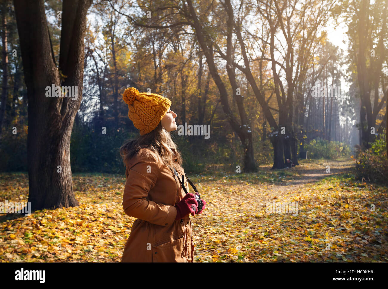 Woman in brown jacket and yellow hat taking a picture with old vintage photo camera at autumn forest Stock Photo