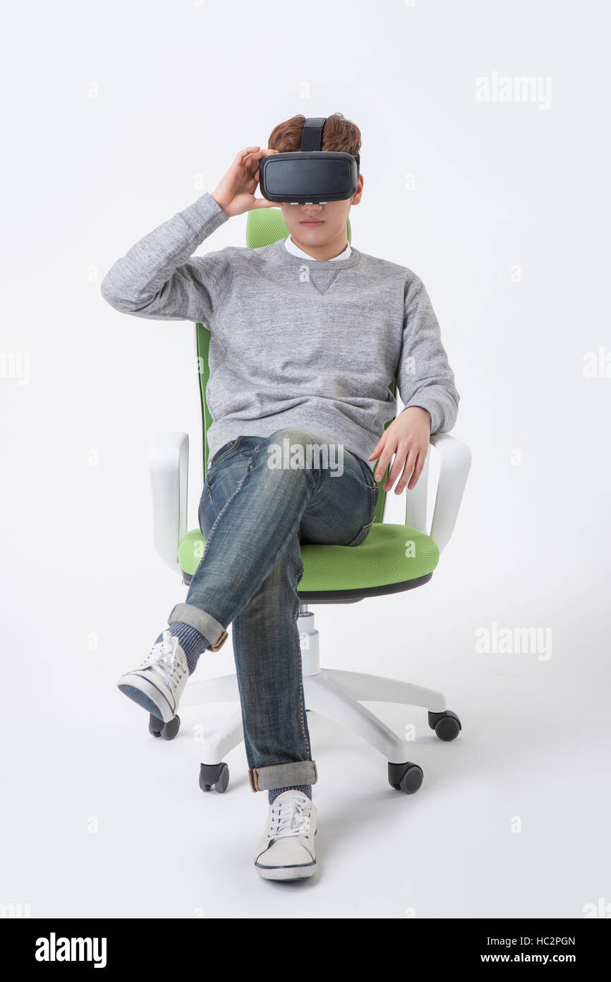 Young Korean man wearing virtual reality headset sitting on chair with his  legs crossed Stock Photo - Alamy