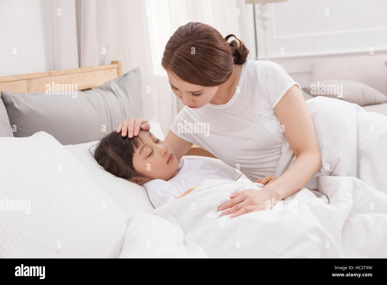 Loving mother putting her daughter to sleep in bed Stock Photo Alamy