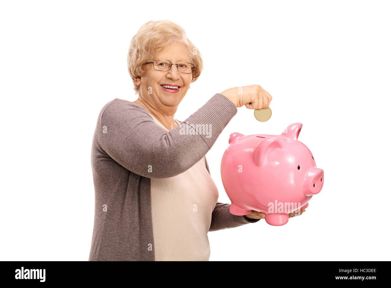 Happy elderly woman putting a coin into a piggybank isolated on white ...