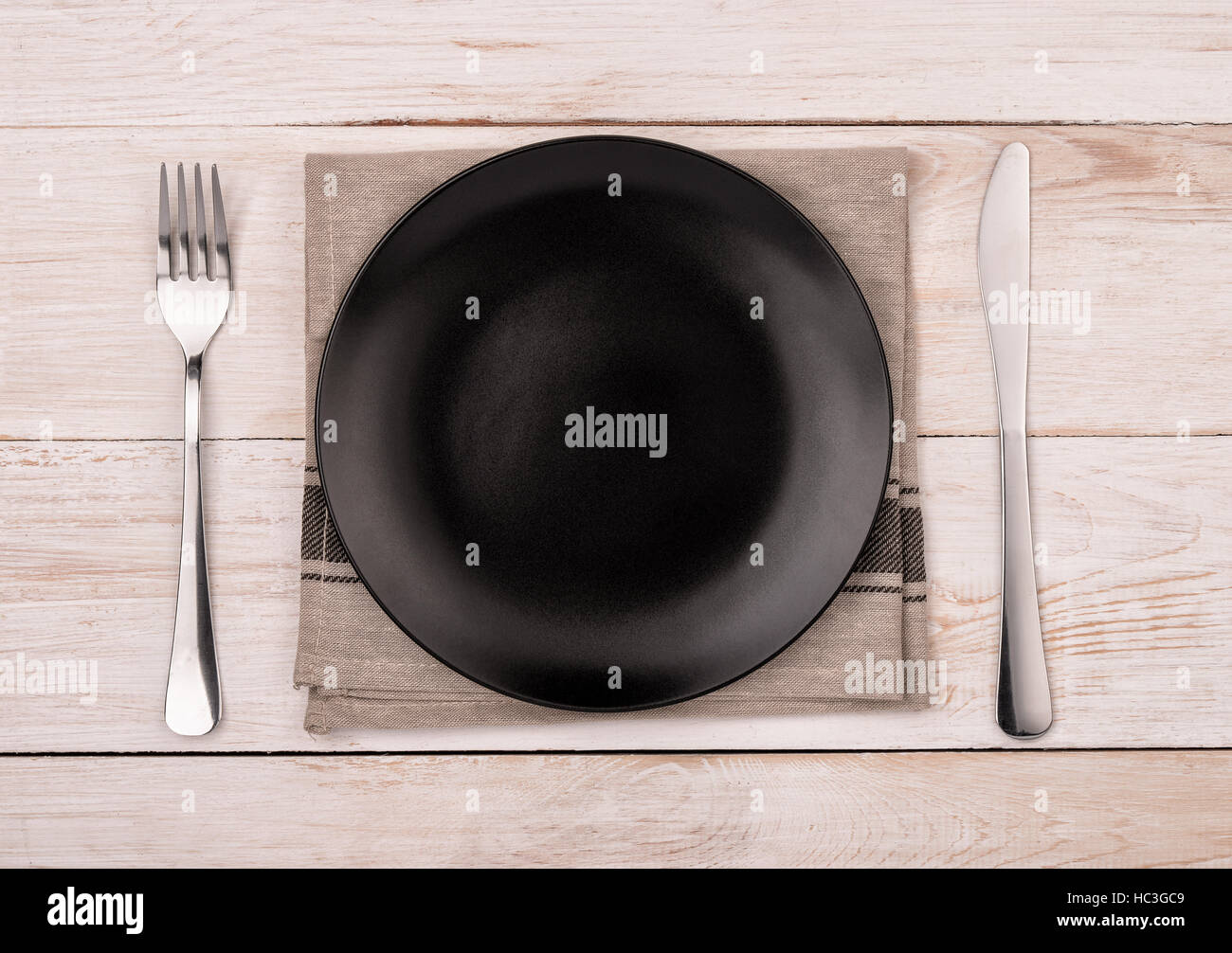 Top view of empty black  plate, silverware and napkin on wooden table background Stock Photo