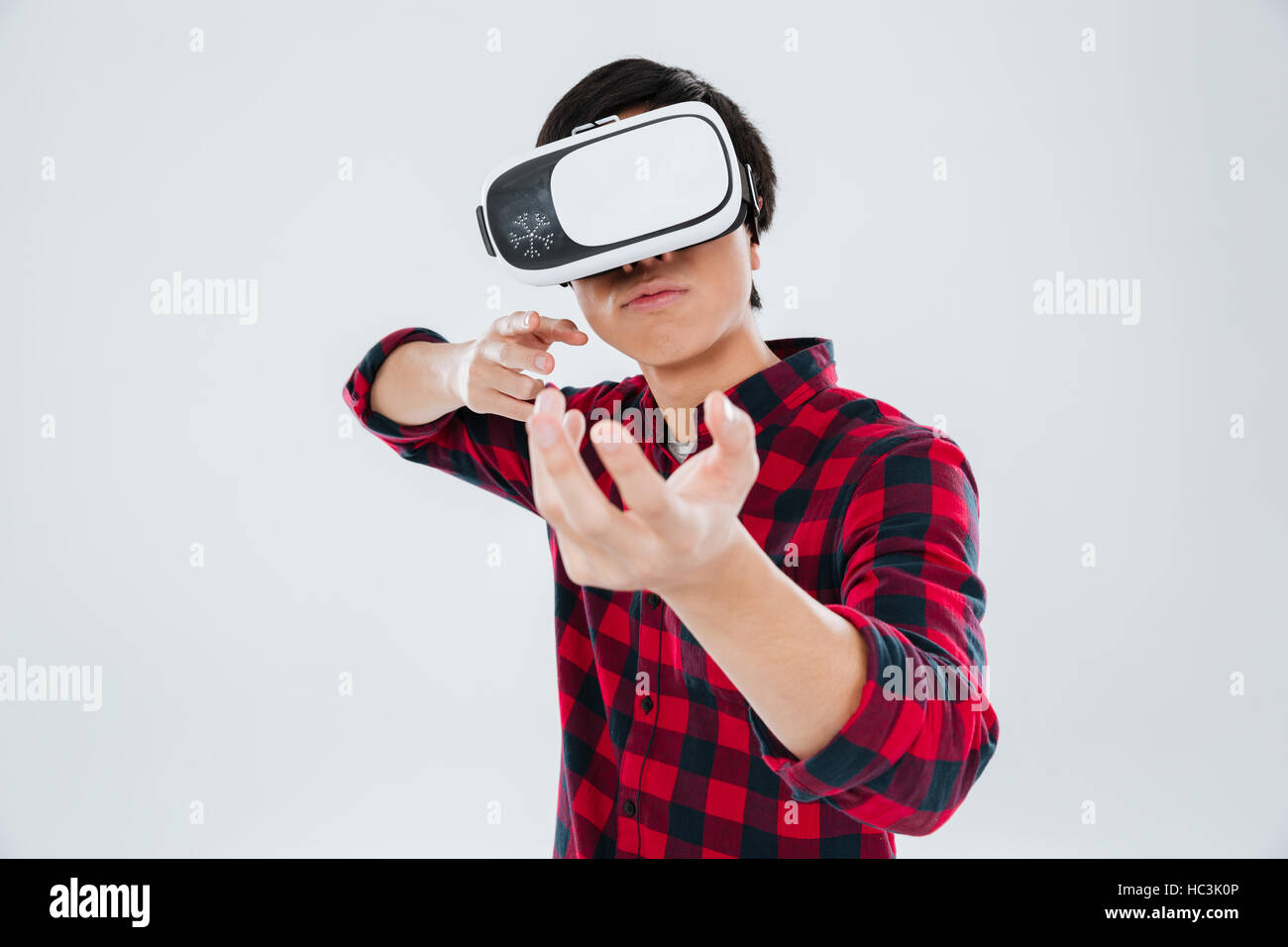 Photo of man dressed in casual shirt in a cage and wearing virtual reality device and holding an imagined gun in hands. Isolated over white background Stock Photo