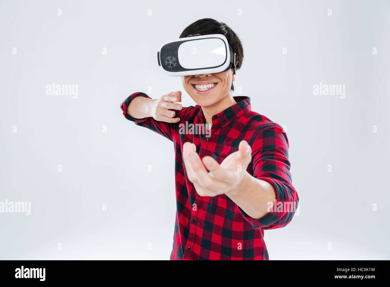 Picture of happy man dressed in casual shirt in a cage and wearing virtual reality device and holding an imagined gun in hands. Isolated over white ba Stock Photo