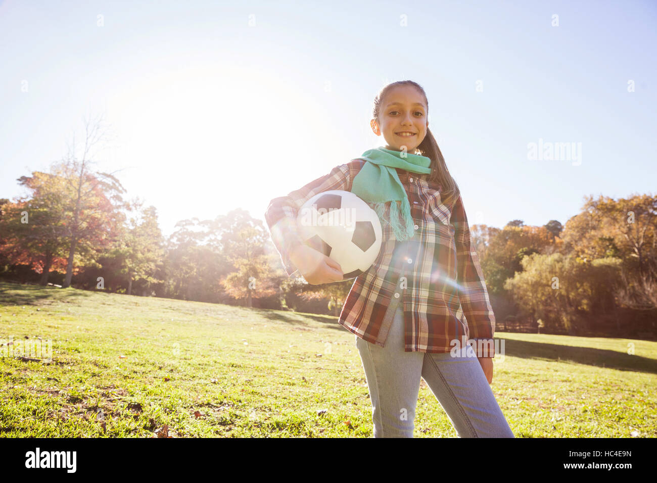 Low angle portrait of smiling girl holding soccer ball in park Stock Photo