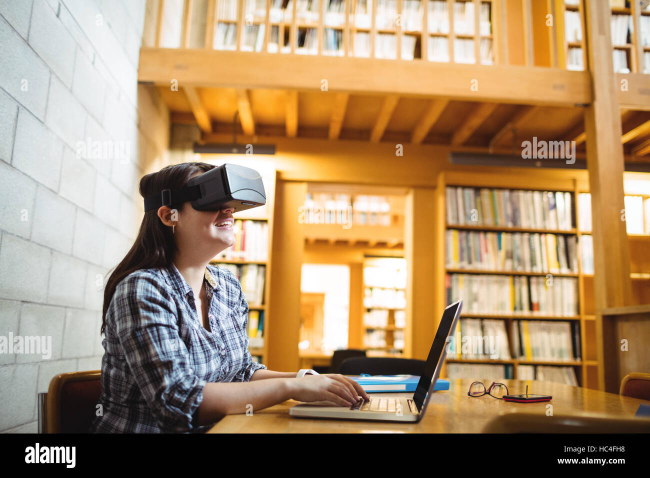 Female student using laptop and virtual reality headset in library Stock Photo