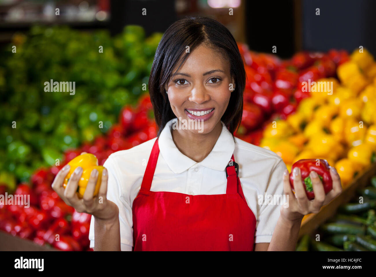 Smiling female staff holding bell peppers in organic section Stock Photo