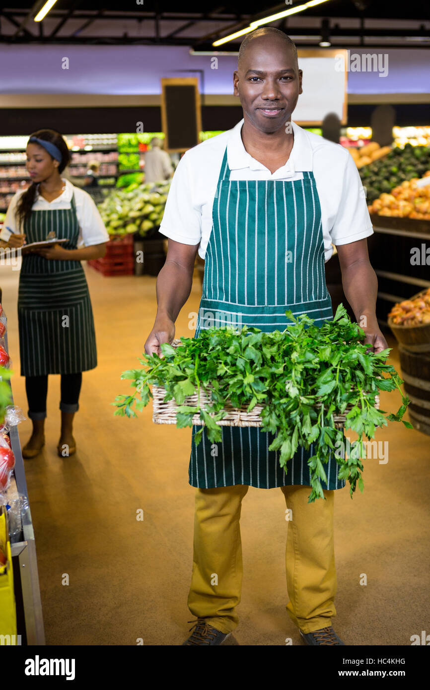 Smiling male staff holding a basket of fresh vegetables at supermarket Stock Photo