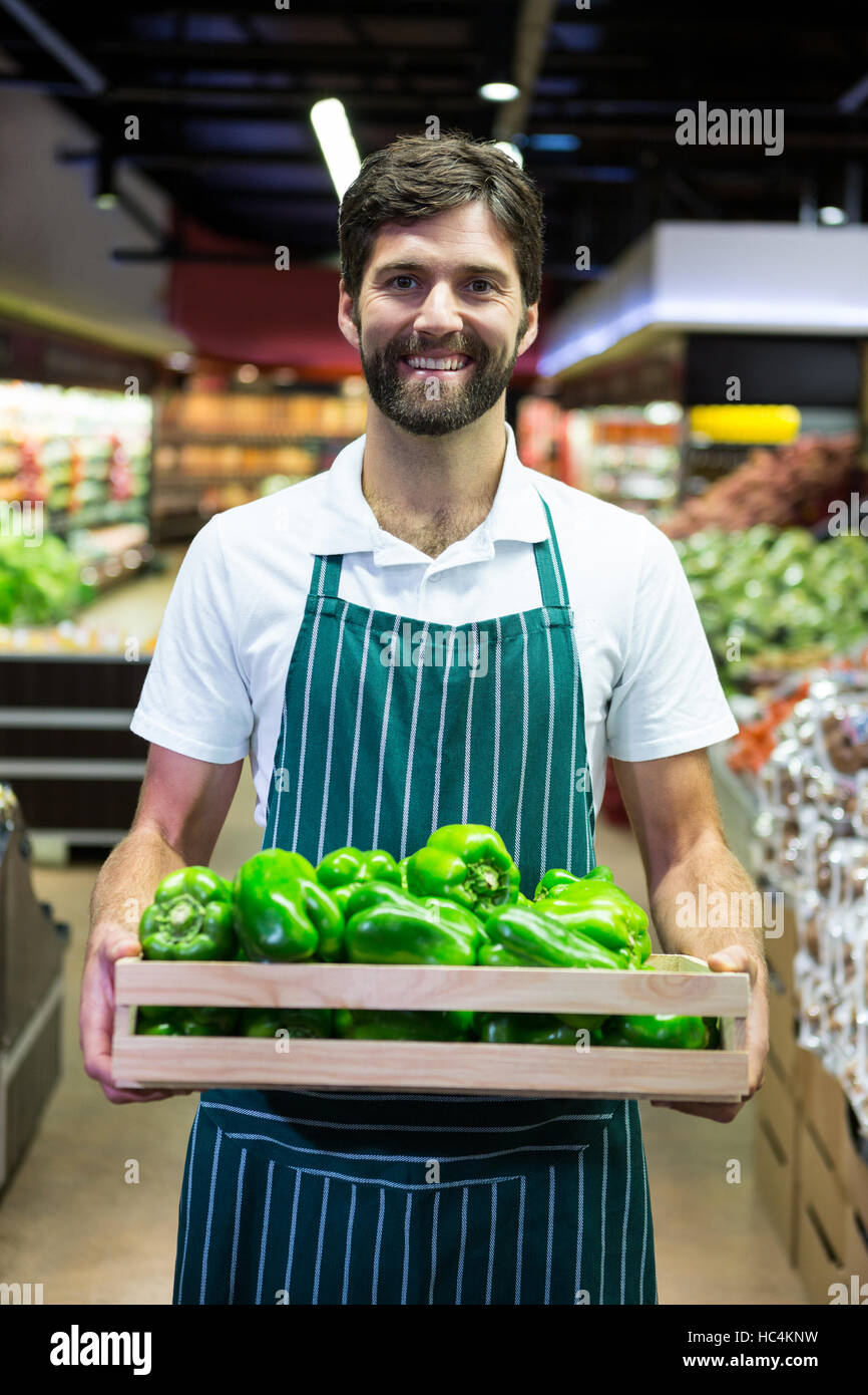 Smiling male staff holding a crate of green bell pepper at supermarket Stock Photo