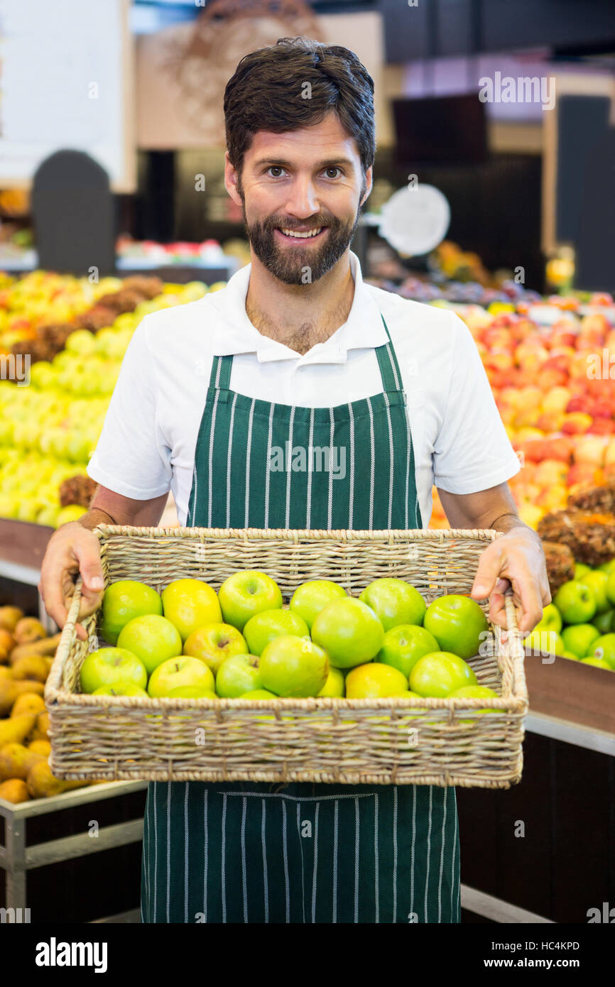 Smiling male staff holding a basket of green apple at supermarket Stock Photo