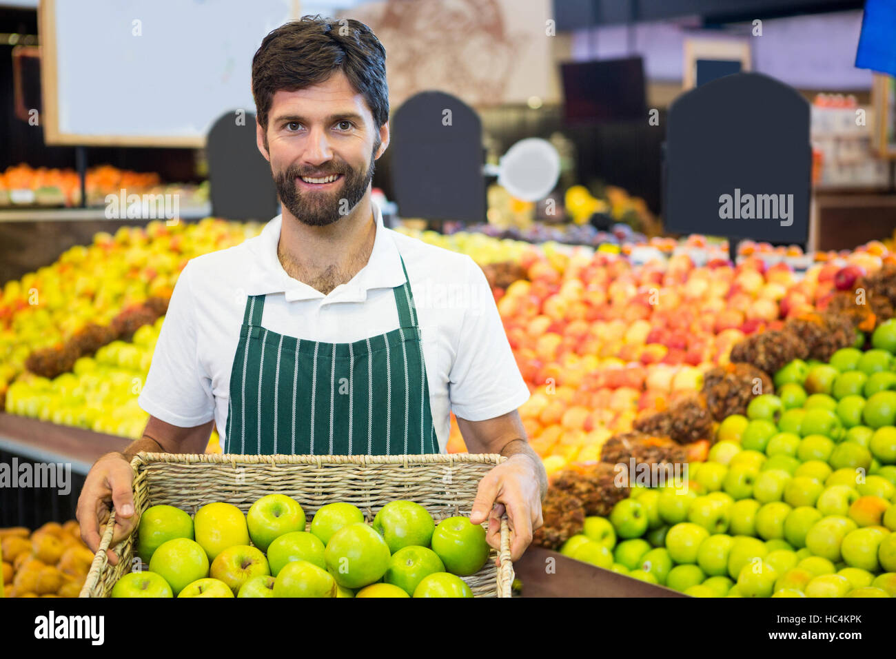 Smiling male staff holding a basket of green apple at supermarket Stock Photo