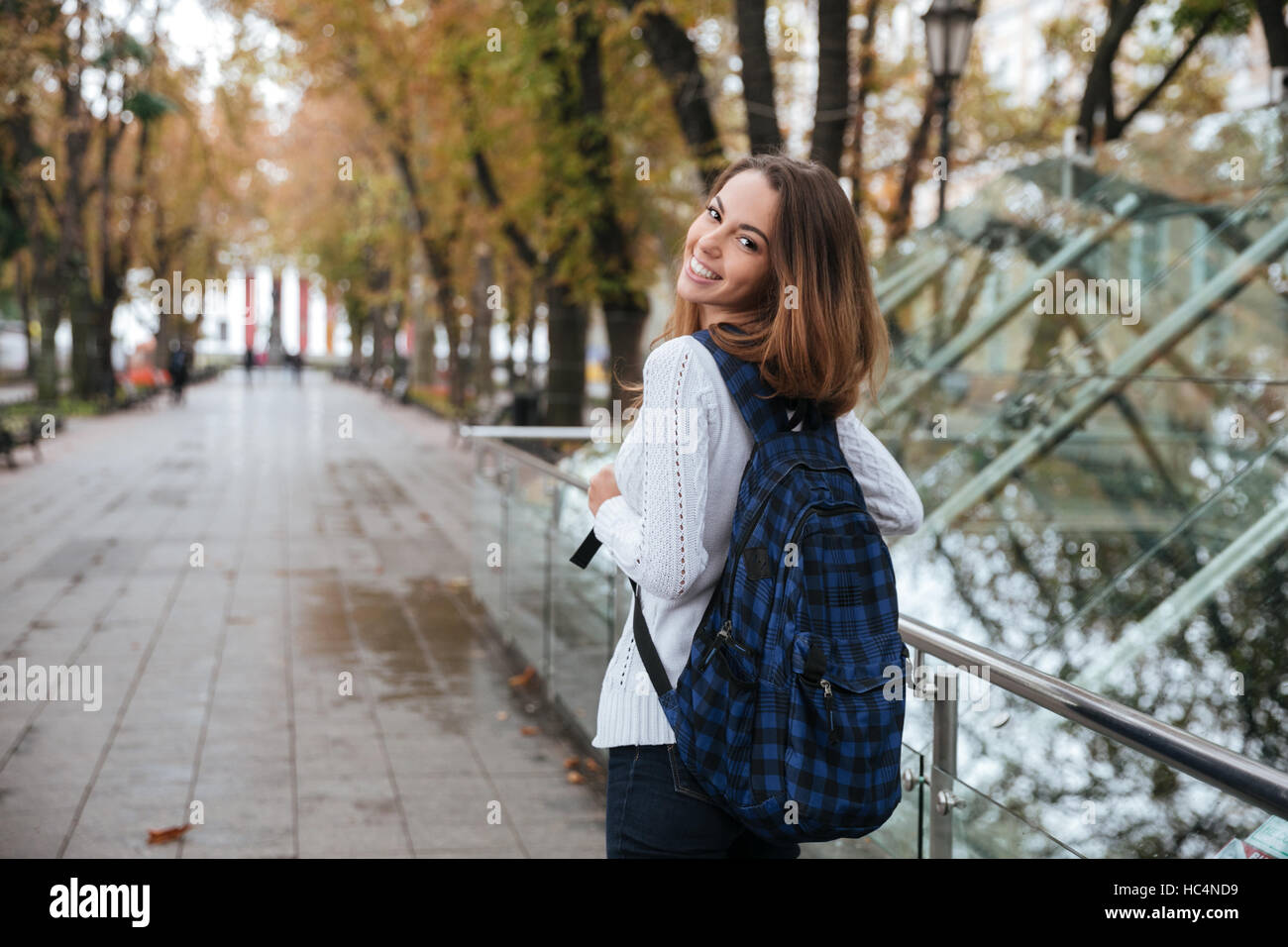 Back view of happy pretty young woman with backpack walking in park ...
