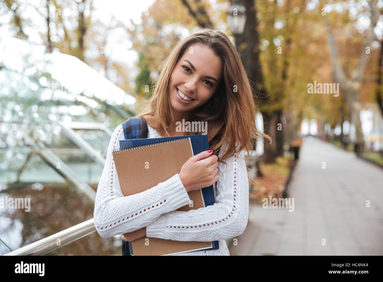 Smiling cute young woman with notebooks standing in park Stock Photo ...