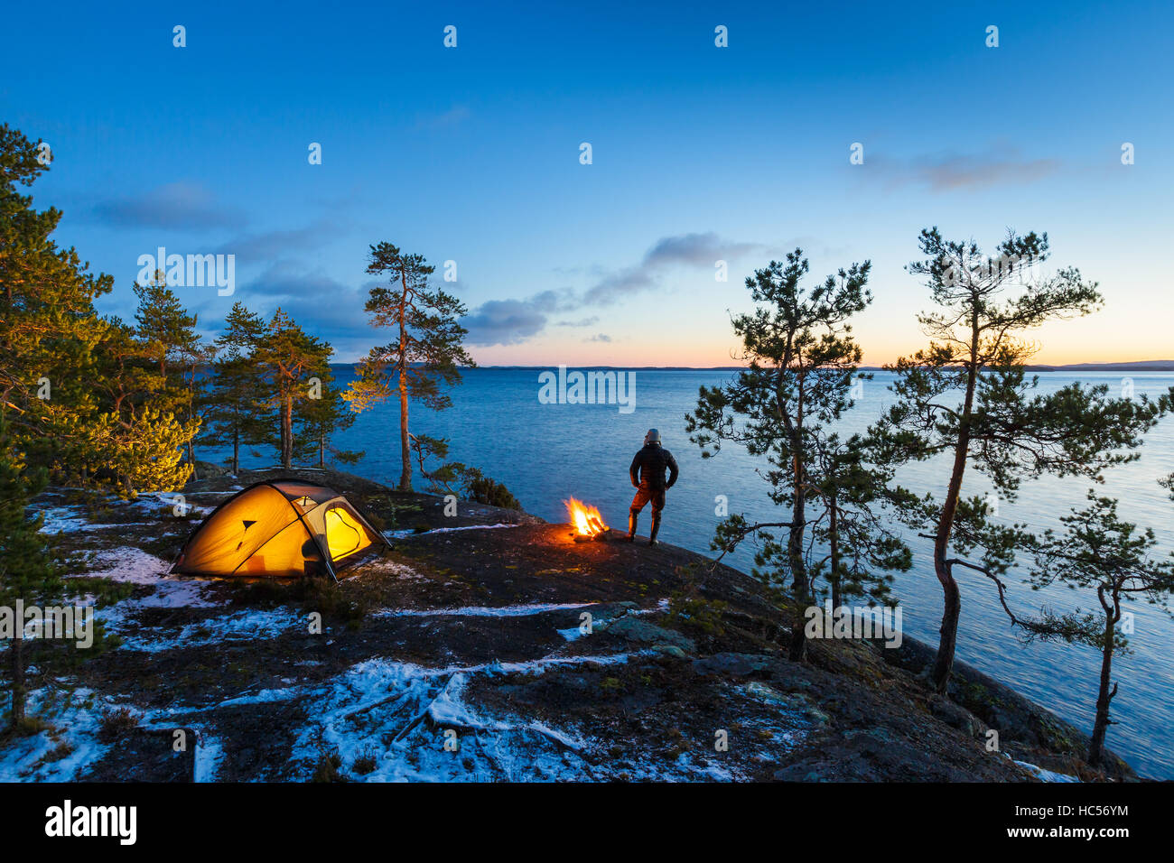 Man is standing around a campfire and just relaxing, snow on the ground Stock Photo
