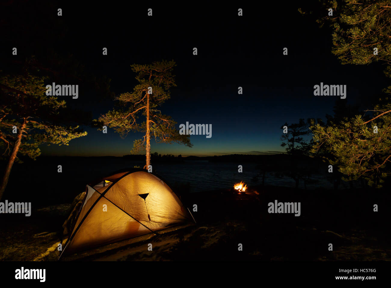 Campfire and tent in wilderness by the lakeside in the night Stock Photo